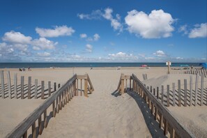 A beach with wooden walkways leading to the water, a lifeguard tower, and beach umbrellas.