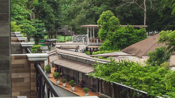 A view of a lush green landscape with a waterfall, a covered outdoor seating area, and a building with a tiled roof. - Namtok Sarika Resotel (Nakhon Nayok)