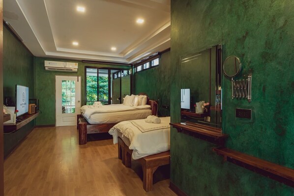 A room with two beds, a mirror, a vanity, and a window with a view of greenery. - Namtok Sarika Resotel (Nakhon Nayok)