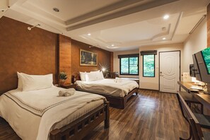 A hotel room with two beds, a desk, a TV, and a window with a view of greenery. - Namtok Sarika Resotel (Nakhon Nayok)