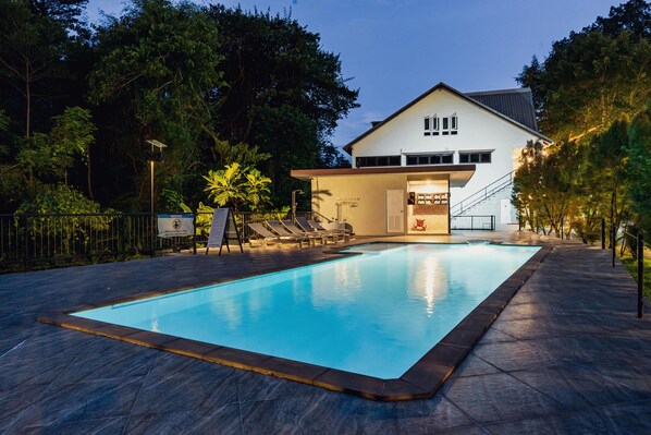 A swimming pool with lounge chairs, a building with a sign, and a staircase leading to the entrance. - Namtok Sarika Resotel (Nakhon Nayok)