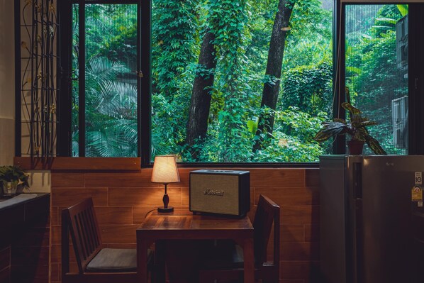 A kitchen with a wooden table, chairs, a radio, and a refrigerator. - Namtok Sarika Resotel (Nakhon Nayok)