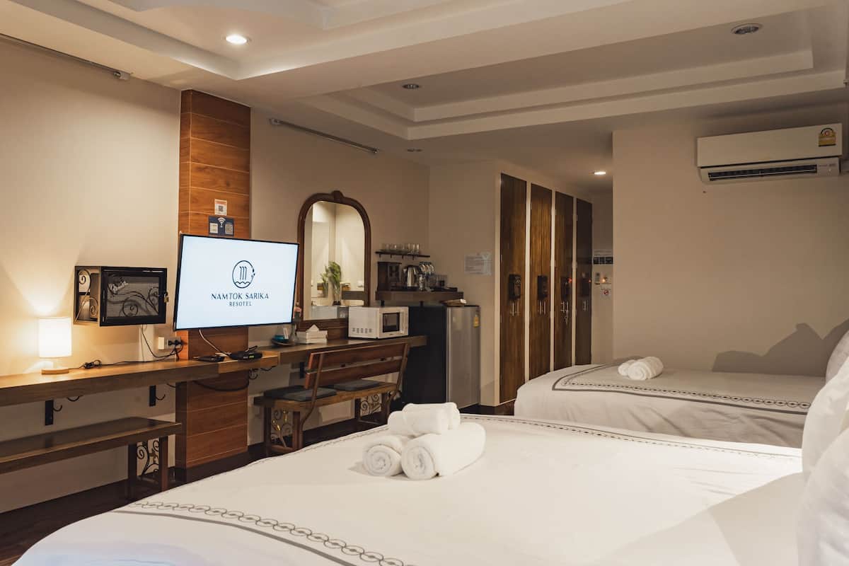 Ein Hotelzimmer mit Schreibtisch, Bett, Fernseher, der den Hotelnamen zeigt, Spiegel, Kleiderschrank und Klimaanlage.