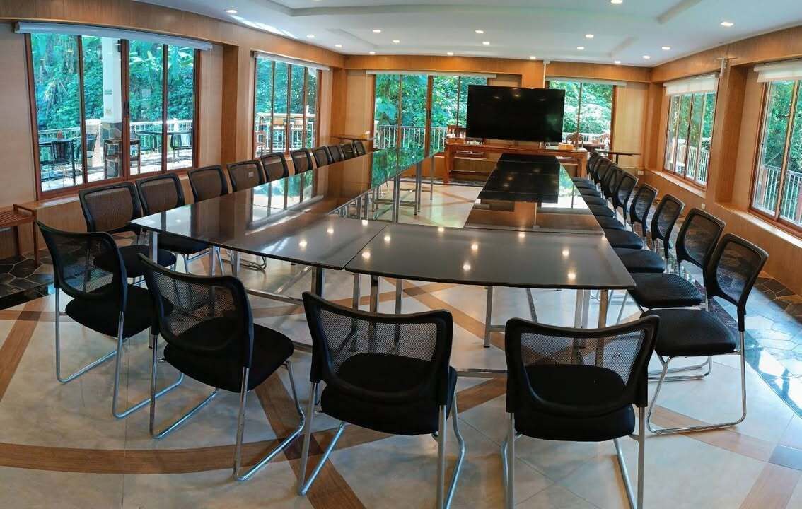 A conference room with a long table and chairs, large windows, and a television.