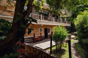A multi-story building with a stone facade, a balcony with a railing, and a paved courtyard with a bench. - Namtok Sarika Resotel (Nakhon Nayok)