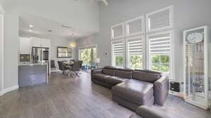 A spacious living area with a large sectional sofa, a dining table with chairs, and a kitchen in the background.