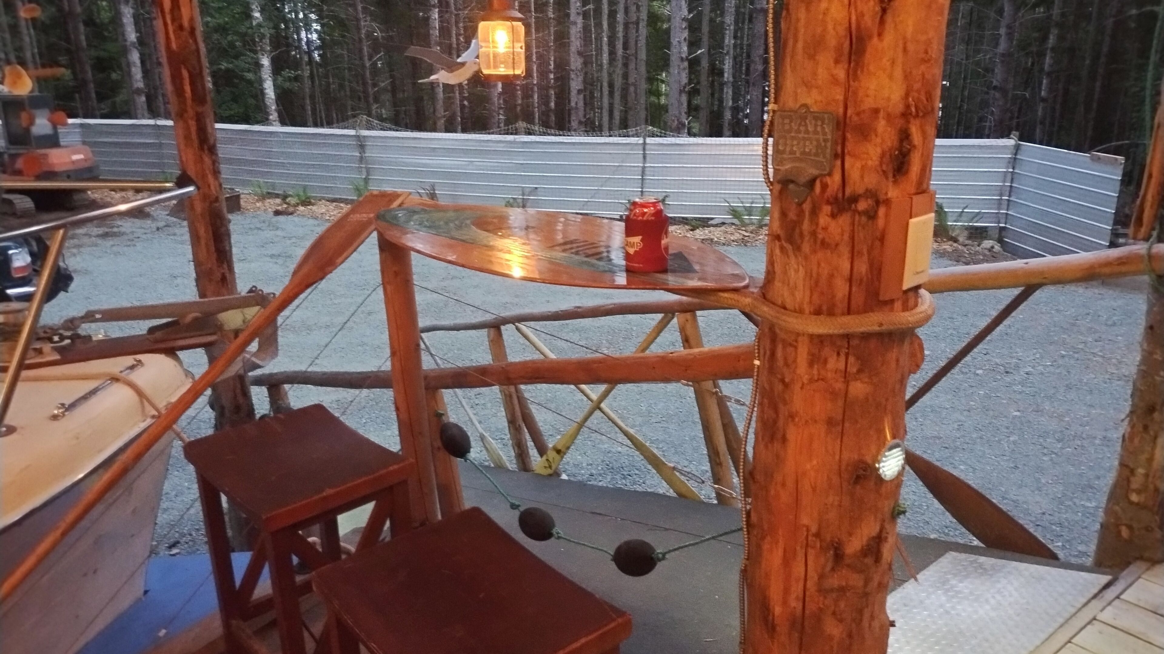 A rustic wooden structure with a glass table and benches, surrounded by a metal fence and trees.