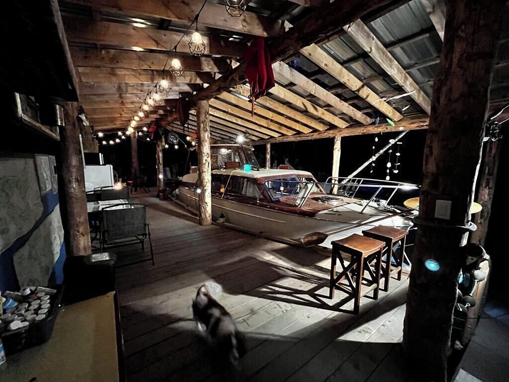 A rustic boat docked inside a wooden building with a high ceiling, wooden floors, and a small table with stools.