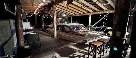 A rustic boat docked inside a wooden building with a high ceiling, wooden floors, and a small table with stools.