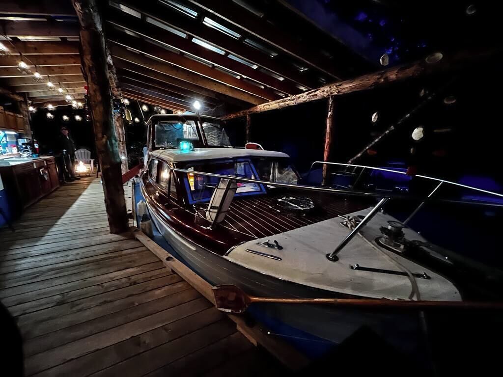 A boat docked inside a wooden structure with a wooden floor and a person standing in the background.