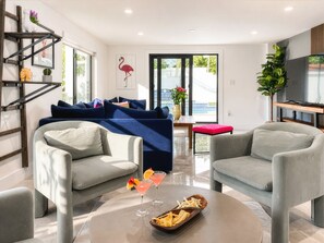 A modern living room with a sofa, two armchairs, a coffee table with drinks and snacks, and a TV on a wooden stand.
