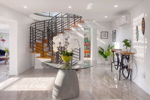 A modern interior with a spiral staircase, a glass table with a vase of white flowers, and a bicycle.