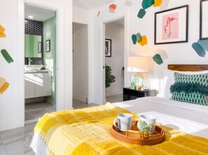 A hotel room with a bed, bedside table, lamp, and a view of the bathroom. - Villa Palma: Heart of Miami | 5 min to Miracle Mile (Miami)