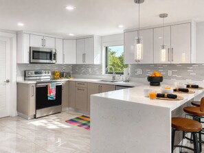 A modern kitchen with white cabinetry, stainless steel appliances, a large island with bar stools, and a colorful rug.