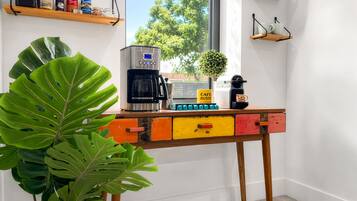 Un coin cuisine équipé d’une machine à café, d’une plante et d’une fenêtre donnant sur des arbres.