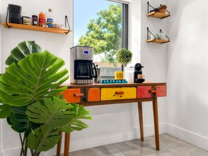 Een keukenhoek met een koffiezetapparaat, een plant en een raam met uitzicht op bomen.