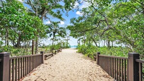 Un sendero arenoso bordeado por árboles y una valla metálica que lleva a una playa.