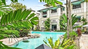 Un hotel con piscina rodeado de exuberante vegetación y un edificio de varios pisos con balcones.