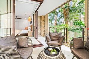 A room with wicker furniture, a bed, and a view of greenery outside.