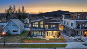 A modern multi-story residential building with a spacious front yard, large windows, and a well-lit entrance.