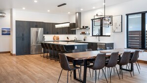 A modern kitchen with a central island, dark cabinetry, and a dining area with a large wooden table and chairs.
