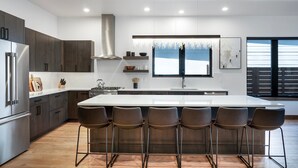 A modern kitchen with a large island, bar stools, and a view of the outdoors.