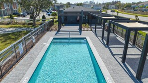 A rectangular swimming pool with a metal ladder, surrounded by a brick walkway and metal fencing.