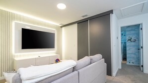 A modern living room with a large flat-screen TV mounted on a wall, a grey sofa, and a white entertainment unit.