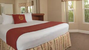Ein Hotelzimmer mit einem großen Bett, einem Holz-Nachttisch, einem an der Wand befestigten Fernseher und einem Fenster mit Blick auf Grünflächen.