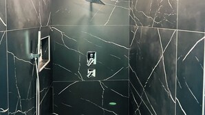 Ein modernes Badezimmer mit schwarzem Marmor an der Wand, einer Duschkabine und einer Deckenleuchte.