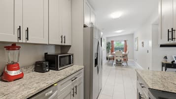 A modern kitchen with white cabinets, a refrigerator, a microwave, a blender, and a dining area with a table and chairs.