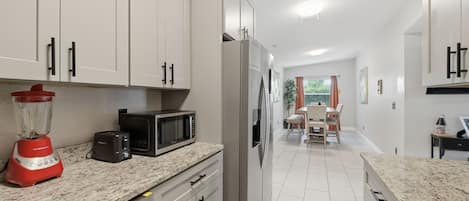 Eine moderne Küche mit weißen Schränken, einem Kühlschrank, einer Mikrowelle, einem Mixer und einem Essbereich mit Tisch und Stühlen.