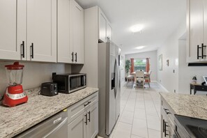 Una cocina moderna con armarios blancos, un refrigerador, un microondas, una licuadora y un comedor con mesa y sillas.