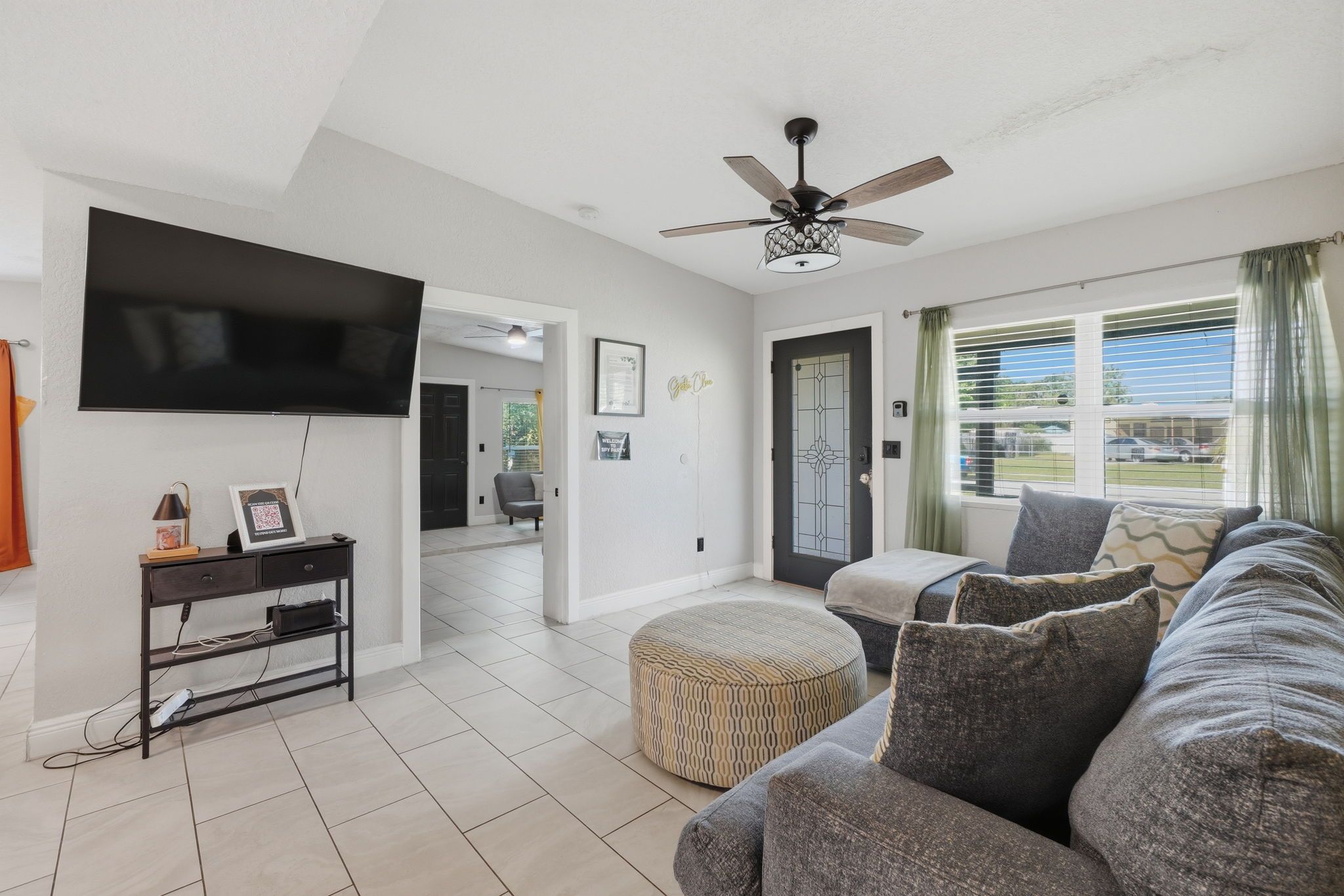 A living room with a flat-screen TV, a ceiling fan, a sofa, and a window with blinds.