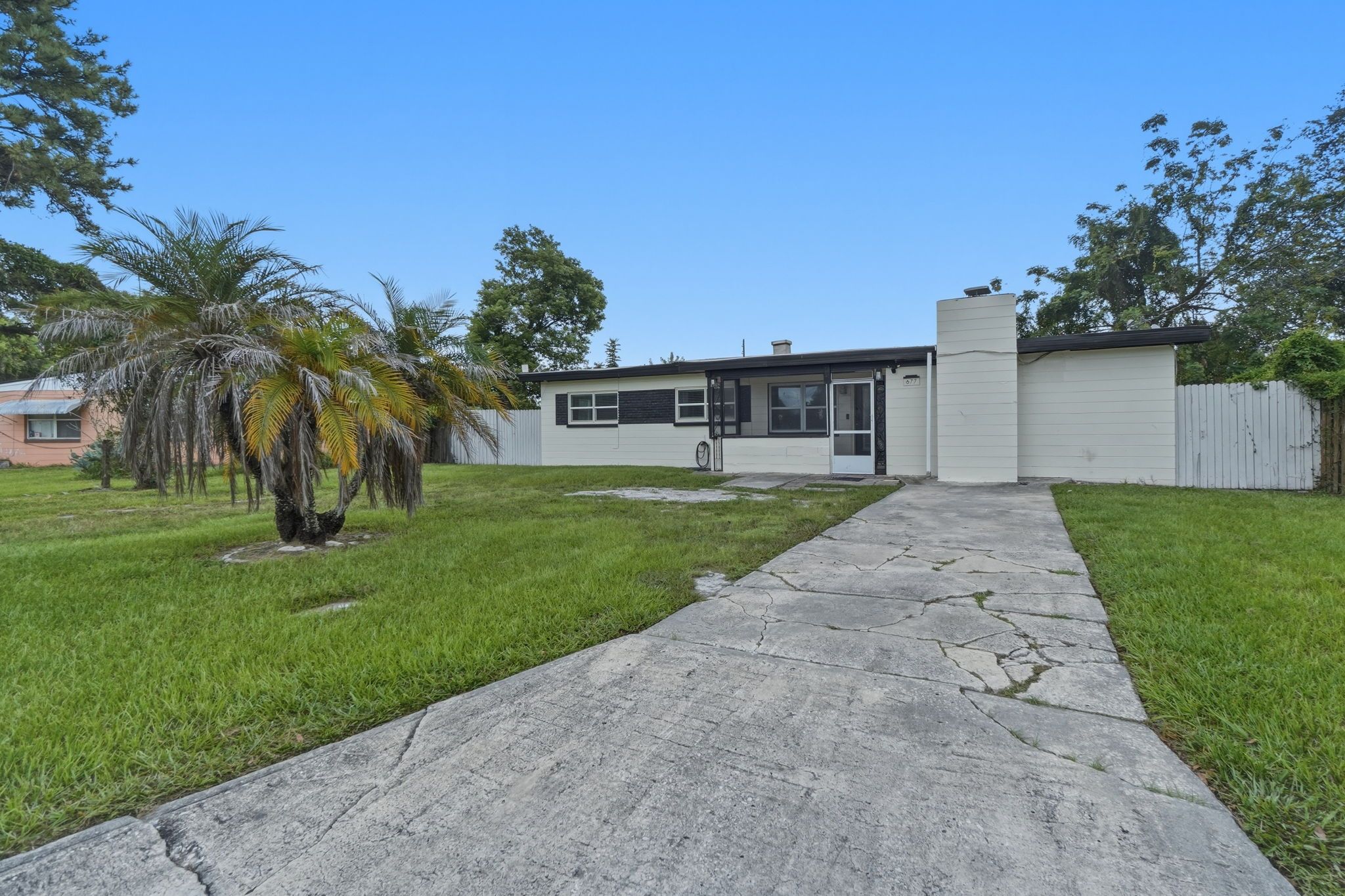 A single-story house with a front yard, a driveway, and a white picket fence.