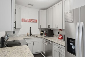 A kitchen with white cabinets, a stove, a coffee maker, and a refrigerator.