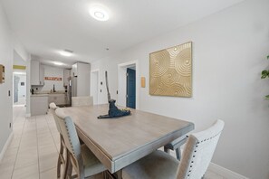 Un comedor con una mesa larga, sillas, una escultura decorativa y una cocina al fondo.