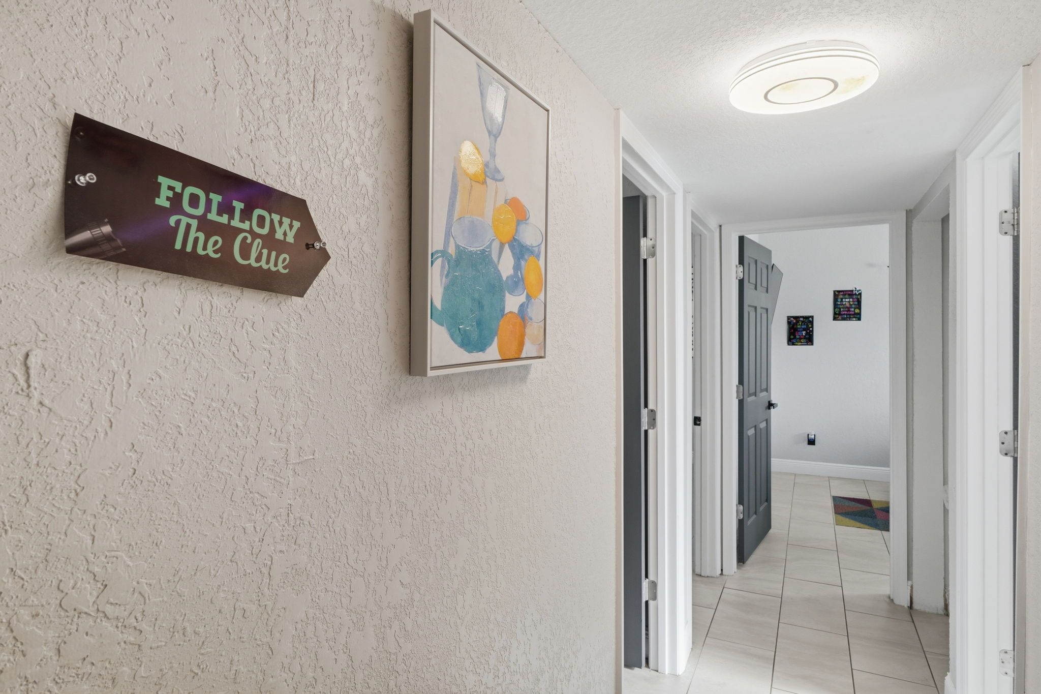 Un pasillo con un cartel que dice 'FOLLOW The Clue' y un colorido cuadro abstracto.