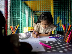 A child writing at a table with colorful pens and pencils, surrounded by a wire mesh and a yellow wall. - Cozy Glamping in Mierlo (Mierlo)