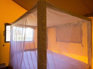 Una habitación con mosquitera sobre la cama y una ventana.