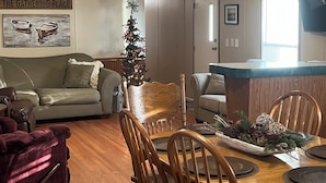 A cozy living room with a green sofa, wooden dining table, and a Christmas tree. - Eagle Lake Escape - lakefront - private lot (Vicksburg)