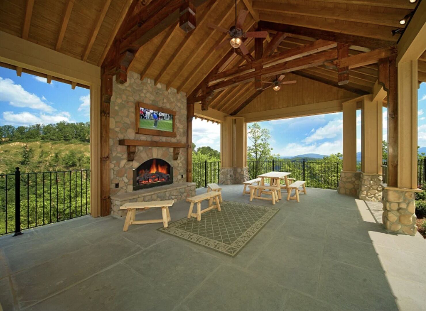 Un patio al aire libre con chimenea de piedra, bancos de madera y un televisor montado sobre la chimenea.