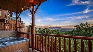 A wooden deck with a hot tub, wooden railings, and a view of mountains.