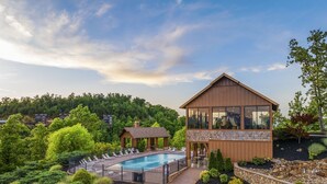 A modern lodge with a large pool, surrounded by lush greenery and a mountainous backdrop.