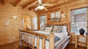 A wooden cabin bedroom with a bed, a nightstand, a ceiling fan, and a window with blinds.