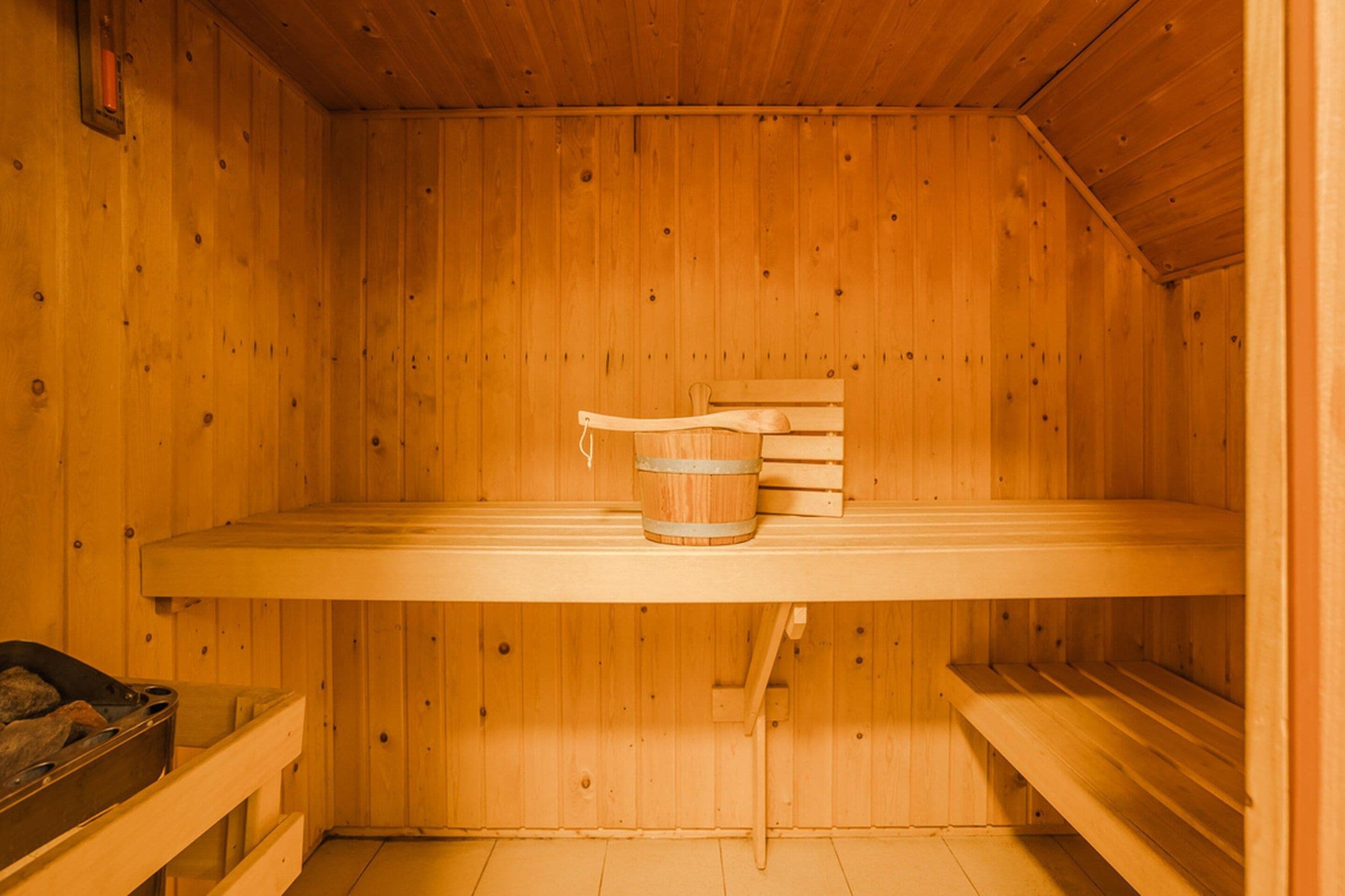 A wooden sauna with benches, a bench with a bucket, and a sauna heater on the wall.