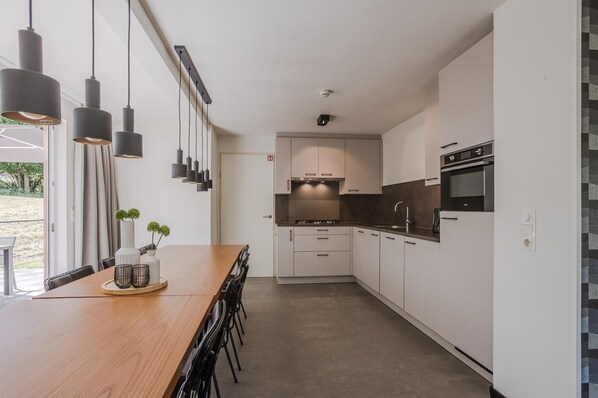 A modern kitchen with white cabinets, a wooden dining table, and pendant lighting.