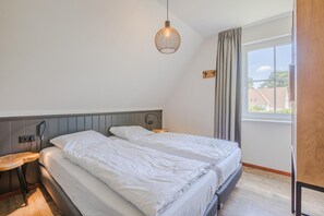 Ett sovrum med två sängar, ett nattduksbord, en lampa, ett fönster med gardiner och utsikt över omgivningen.