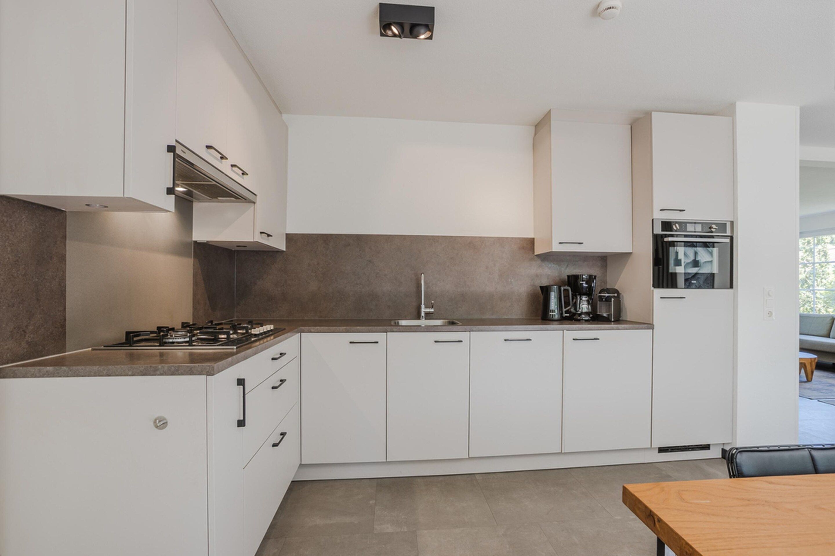 A modern kitchen with white cabinetry, a gas stove, a coffee maker, and a built-in oven.