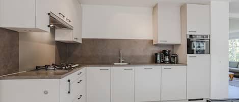 A modern kitchen with white cabinetry, a gas stove, a coffee maker, and a built-in oven.